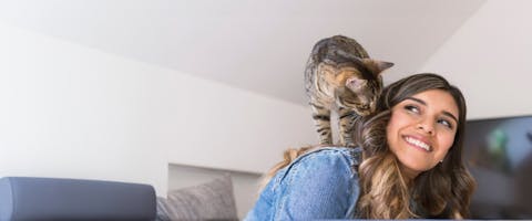 A smiling cat sitter with a tabby cat sitting on her shoulder.